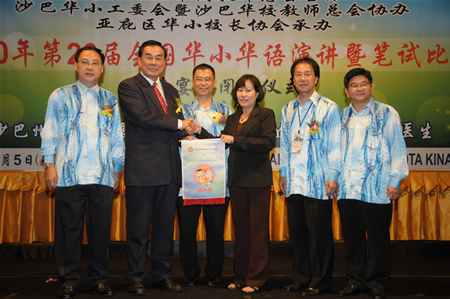 教总主席移交第27届全国华小华语演讲暨笔试赛旗帜予玻璃市州代表。左一起：沙巴教总主席拿督黄天亮校长、教总主席王超群、沙巴州资源发展及资讯工艺部长拿督于墨斋医生、玻璃市州代表黎明珠校长、沙巴发展华小工委会主席周惠卿，以及沙巴华小校长协会主席陈俊豪校长。